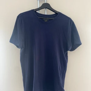 Mörkblå Ralph Lauren T-shirt - En stilren mörkblå t-shirt från Polo Ralph Lauren i mjuk bomull. Klassisk passform med rund halsringning och korta ärmar. Diskret broderad logga i vitt nertill på framsidan. Perfekt för en clean och enkel look.