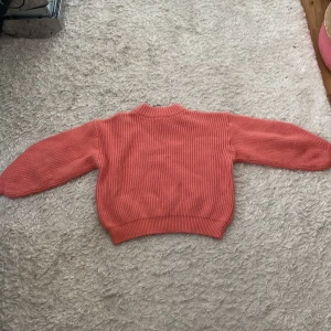 Rosa ribbstickad tröja med lång ärm - Säljer en rosa ribbstickad tröja med lång ärm och rund hals. Tröjan har en croppad passform och breda muddar vid ärmslut och nederkant. Perfekt för lager på lager och ger en chill vibe till din outfit.