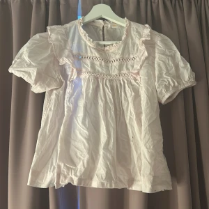 Ljusrosa blus med volangdetaljer - Supersöt ljusrosa blus med korta puffärmar och volangdetaljer på axlarna. Blusen har rund halsringning, dekorativa broderier framtill och knapp i nacken ( jag tvättar bort all smuts på den innan jag skickar den!💕