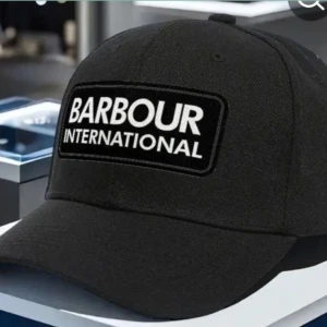 Svart keps från Barbour International - Snygg svart keps från Barbour International med tydlig vit logga framtill. Klassisk böjd skärm och justerbar passform. Perfekt accessoar för en sportig och stilren look. Postar samma dag vid köp och sista kvar så passa på! 