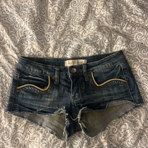 Jeansshorts från Blue Collection - Snygga mörkblå jeansshorts från Blue Collection med råa, fransiga kanter och coola detaljer vid fickorna. Klassisk femficksmodell med kontrastsömmar och låg midja. Perfekta för sommardagar när du vill ha en avslappnad och trendig look.