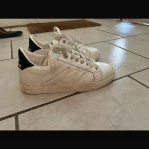 Vita sneakers från Zadig & Voltaire - Snygga vita sneakers från Zadig & Voltaire med blixtdetalj på sidan. Skorna har snörning och är tillverkade i skinn . Använda en gång på en fest så de är inte slitna utan bara smutsiga så det går att tvätta bort 💕 nypris:3450