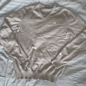 Ljusgrå v-ringad tröja från J.Lindeberg - Säljer en stilren ljusgrå v-ringad tröja från J.Lindeberg i merinoull med diskret logga på bröstet. Tröjan är tunnstickad och har långa ärmar samt ribbade muddar vid ärmslut och nederkant. Perfekt för lager-på-lager och enkel att matcha. Nypris- 1400kr