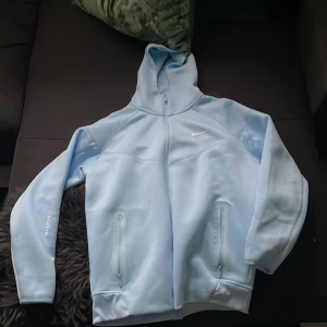 Ljusblå hoodie från Nike x NOCTA - Säljer min NOCTA fleece pågrund av att jag köpte fel storlek. Lätt den skönaste hoodien jag haft och även fin blå färg. Endast använd en gång. Det är bara att skriva om ni har frågor!