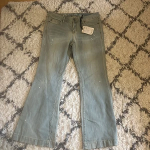 Ljusblå bootcut jeans  - Ljusblå bootcut jeans med unika detaljer ifrån converse one star. Ny med prislapp, lite slitningar vid benänden som är del av designen. Midjemått: 43 cm. Innerbenslängd: 80 cm.