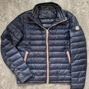 Mörkblå dunjacka från Moncler - Säljer just nu min riktig feta moncler jacka som är i storlek fem men sitter som M-L | Jätte bra skick med ett pyttelitet skräddarlagat hål men man ser inget vid användande. om du har några frågor eller vill se bild på de deffekten så får du gärna höra av dig. Jag tar som vanligt jättegärna byten och då möts jag i Stockholm.