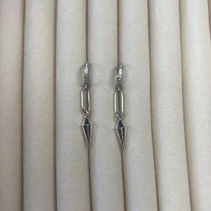 Silverfärgade örhängen med spetsig hängande detalj - Säljer ett par stilrena silverfärgade örhängen med små gnistrande stenar på ringen och en spetsig, avlång hängande detalj. Perfekta för dig som gillar minimalistisk och modern design.