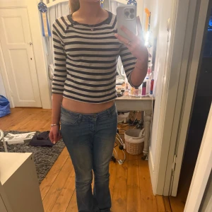 Randig topp från Polo Ralph Lauren - Säljer en topp från Polo Ralph Lauren i marinblått och vitt med horisontella ränder. Toppen har trekvartsärm och dekorativa knappar vid axeln. Perfekt för dig som gillar en najs passform och klassisk stil.