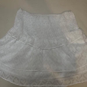 Vit kortkjol med volang från Gina Tricot🤍 - Säljer en söt vit kortkjol från Gina Tricot med bred smock i midjan och volangdetalj upptill. Kjolen har ett diskret mönster i tyget och är perfekt för varma dagar. Superfin att matcha med en enkel topp! Pris kan såklart diskuteras, frågor eller fler bilder hör av dig, kjolen passar xs och s!🤍💕
