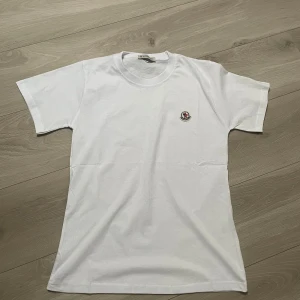Vit t-shirt från Moncler - Klassisk vit t-shirt från Moncler med rund halsringning och liten broderad Moncler-logga på bröstet. Enkel och stilren design i mjuk bomull som passar perfekt till jeans eller shorts.