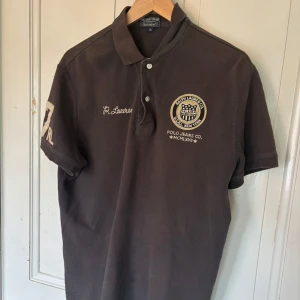 Ralph Lauren pike  - Säljer en brun pikétröja från Ralph Lauren i storlek M. Tröjan har korta ärmar, krage och knappar framtill. Broderade detaljer på bröstet och ärmen med siffran 67 och RL. Perfekt för en trendig och stilren look.💯