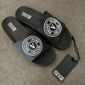 Äkta Versace - Jeans Corture tofflor - Helt nya och äkta Versace - Jeans Corture tofflor. Medföljer tagg. Storlek 45, passar även 44.