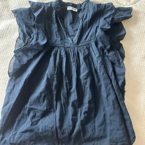 Mörkblå blus med volang från Meet Me There - Säljer en mörkblå blus från Meet Me There i storlek S/M. Blusen har v-ringning, volangdetaljer längs ärmarna och är tillverkad i ett lätt och luftigt tyg. Perfekt för vår och sommar!