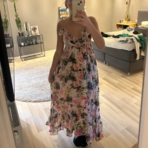 Blommig långklänning med volang - Fin långklänning med blommigt mönster i rosa, grönt och beige toner. Klänningen har smala axelband, volangdetaljer vid bysten och en luftig passform. Perfekt för sommarens alla tillfällen.