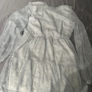 Ljusblå blommig klänning från NLY Trend - Säljer en söt ljusblå klänning från NLY Trend med diskret blommigt mönster. Klänningen har långa ärmar, volangdetaljer och en lätt rynkad midja. Perfekt för vår och sommar!