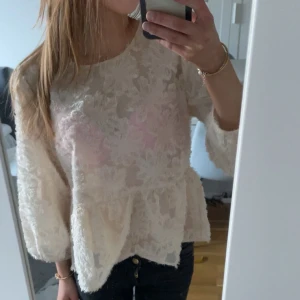 Vit spetsblus med volang - Säljer en söt vit blus med spetsdetaljer och volang nertill. Blusen har trekvartsärm och en lös passform, perfekt för en romantisk look. Passar lika bra till jeans som till kjol💗