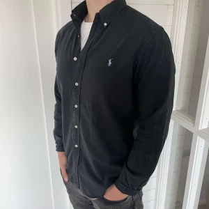 Ralph lauren skjorta - En riktigt fet svart polo ralph lauren med ljusblå loga i bra skick och storlek L slim fit. Hör av er vid frågor.