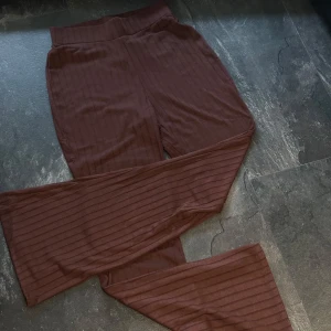Bruna ribbade byxor från Ellos - Mörkbruna ribbade byxor från Ellos med utsvängda ben och hög midja. Byxorna har en mjuk och stretchig känsla, perfekta för en avslappnad och trendig stil. Snygga att matcha med en enkel topp eller hoodie. Byxan är helt ny med prislapp kvar! 