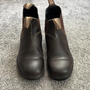Bruna boots från Blundstone - Säljer ett par klassiska bruna Blundstone boots i skinn med elastiska paneler på sidorna och dragflikar fram och bak. Perfekta för dig som vill ha en tidlös och robust sko med rund tå och platt sula.