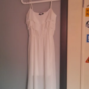 Vit långklänning med volang från Bik Bok - Säljer en vit långklänning från Bik Bok med smala axelband och volangdetaljer upptill. Klänningen har en luftig och flowy passform, perfekt för varma dagar. Enkel och stilren design som känns fräsch och somrig.