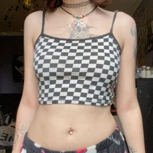 Svartvit rutmönstrad croppad linnetopp - Säljer en croppad linnetopp med svartvitt rutmönster och tunna axelband. Perfekt för dig som gillar en edgy och trendig stil. Finns några svarta fläckar på väldigt små 