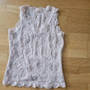 Beige spetslinne från Buch Copenhagen  - Säljer ett romantiskt beige spetslinne från Buch Copenhagen. Linnet är ärmlöst och har vacker blommig spets över hela plagget samt en lätt vågig kant nertill och vid halsringningen. Guldfärgade detaljer. Framsidan fodrad,,ryggen är genomskinlig. Som en ny !