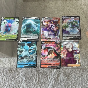 Pokémon V-kort samling - En färgstark samling av sex Pokémon V-kort och ett tränarkort. Perfekt för dig som gillar att samla, byta eller spela Pokémon TCG. Korten har coola illustrationer och glänsande detaljer som gör dem extra attraktiva för unga samlare.