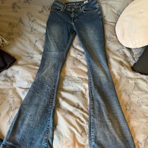 Blå low flare jeans med låg midja - Säljer ett par blå jeans med låg midja och flare-ben. Modellen är 'low flare' och byxorna har klassisk femficksdesign, knapp och dragkedja framtill. Passar dig som gillar en tight passform upptill och utsvängda ben. Midjemått XS, längd 32. De är använda  och vart för långa på mig vilket gjort så att de blivit lite slitna nere i benen.