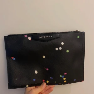 Svart kuvertväska från Givenchy med färgglada prickar - Säljer en svart kuvertväska från Givenchy med färgglada prickar i olika storlekar. Väskan har dragkedja upptill och Givenchy-logga framtill. Nummer: TE1103