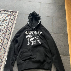 Svart hoodie från Amstaff med tryck - Säljer en snygg amstaff hoodie i storlek L de är liten i storleken, den är helt ny har bara testat den på om du har några frågor eller funderingar tveka inte på att höra av er