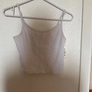 Vit ribbad linnetopp från FB Sister - Säljer en vit ribbad linnetopp från FB Sister i storlek S. Toppen har smala axelband och är croppad, perfekt för varma dagar eller som layering-plagg. Enkel och stilren design som passar till mycket.