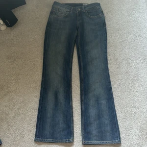 Blå jeansbyxor från Tommy Hilfiger - Snygga blå jeansbyxor från Tommy Hilfiger med klassisk femficksdesign och raka ben. Byxorna har subtila slitningar och kontrastsömmar på bakfickorna. Passar perfekt till en avslappnad stil.