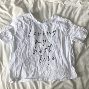 Vit t-shirt med text  - Vit t-shirt från River Island med svart text på framsidan där det står 'Living my best life'. T-shirten har rund halsringning och korta ärmar. Perfekt för en avslappnad och stilren look.