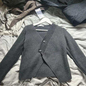 Mörkgrå omlottkofta från Zara - Säljer en mörkgrå stickad omlottkofta från Zara . Använd 1 gång