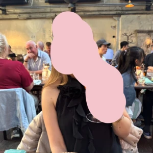 Svart mesh linne med volang och rosett - Svart ärmlös blus med volangdetaljer framtill och en rosett/blomma vid halsen 🖤 Skört material som är lite see through i ryggen men ej på framsidan! Så snygg!