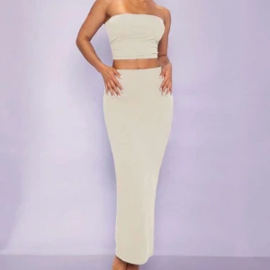 Beige tvådelad långklänning med tubtopp - Säljer en stilren tvådelat set i beige med tubtopp och lång, figurnära kjol. Perfekt för dig som gillar minimalistisk och trendig stil. Kjolen är stretchig och toppen är axelbandslös.