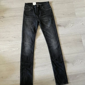 Svarta jeans High Kai från Nudie Jeans - Säljer ett helt nytt par svarta jeans från Nudie Jeans, modell High Kai. Jeansen har smal passform och klassisk femficksdesign med orangea detaljer. Storlek W28 L34. Perfekta för dig som gillar en stilren och tidlös look.