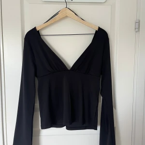 Svart långärmad topp med v-ringning och knyt  i ryggen - Säljer en svart långärmad topp med djup v-ringning både fram och bak. Toppen har ett snyggt knytband i ryggen som ger en extra detalj. Perfekt att styla till olika outfits.