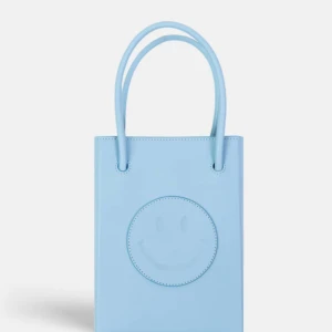 The Case Factory - Essential Crossbody Väska Smiley Vegetable Tanned Light Blue - Säljer en ljusblå  väska från The case factory med smiley på framsidan. Väskan har två handtag och en stilren, rektangulär form. Perfekt för dig som vill ha en rolig och trendig accessoar till din outfit. Axelband medkommer ej. Aldrig använd, nypris 2990 sek