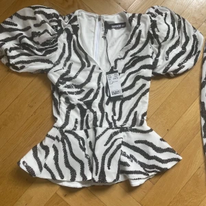 Vit och svart zebramönstrad topp med kjolfrån Rotate  - Säljer en vit topp plus en kjol från Rotate med svart zebramönster och puffiga korta ärmar. Toppen kommer med kjolen. Materialet är glittrigt och ger en festlig känsla, säljer även matchande kjol. (Aldrig använts)💞