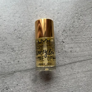 NYX Honey Dew Me Up Primer - NYX Honey Dew Me Up Primer med guldglitter i genomskinlig gelformula. Kommer i en liten glasflaska med guldfärgat lock. Perfekt för att ge huden lyster innan smink. Den är inte använd men den är öppnad. 