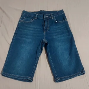 Blå jeansshorts med klassisk femficksdesign - Säljer ett par blå jeansshorts med normal passform och klassisk femficksdesign. Shortsen har dragkedja och knapp framtill samt bakfickor. Perfekta för en avslappnad stil under varmare dagar.