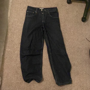 Baggy Mörkblå jeans från BDG Urban Outfitters - Säljer ett par mörkblå jeans från BDG Urban Outfitters med broderad bakficka och baggy. Klassisk femficksmodell med knapp. Storlek 29W 32L.