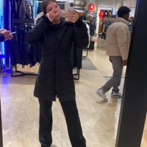 Svart Lorette Parka från Canada Goose - Säljer en svart Lorette Parka från Canada Goose. Jackan är lång med huva och har klassisk pufferdesign med knappar och dragkedja framtill. Perfekt för kalla dagar med sin varma och stilrena look.