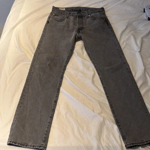 Gråa Levi's 501 jeans - Säljer ett par klassiska gråa Levi's 501 jeans med raka ben och fem fickor. Jeansen har knappgylf och den ikoniska läderpatchen bak i midjan. Perfekta för dig som gillar en tidlös och avslappnad stil.