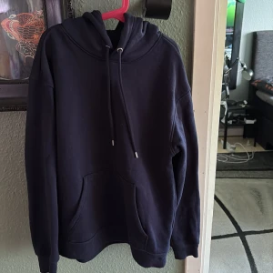 Mörkblå hoodie från H&M - Säljer en mörkblå hoodie från H&M i loose fit-modell. Tröjan har huva med dragsko och en stor magficka framtill. Perfekt för en avslappnad stil och enkel att matcha med andra plagg.