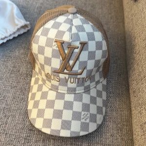 Rutig keps  - Snygg keps med rutigt mönster i beige och vitt, samt stora broderade LV-bokstäver framtill. Kepsen har mesh på sidorna och baksidan för extra ventilation. Perfekt accessoar för en trendig look. Bara att skriva vid frågor och priset kan diskuteras!