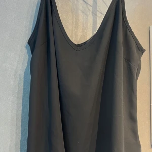 Svart ärmlös klänning med v-ringning - Enkel och stilren svart linne med djup v-ringning och tunna axelband. Linnet har en lös passform och är perfekt för varma dagar eller att styla med accessoarer. Storlek m men passar även s 