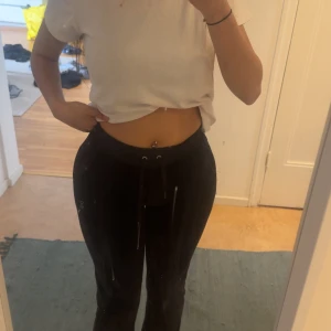 Svarta velourbyxor från Juicy Couture - Säljer ett par klassiska svarta mjukis  från Juicy Couture med snörning i midjan och glittrig 'Juicy'-text bak. Byxorna har en mjuk känsla och normal passform, ett litet hål vid ena knät, kan sy ihop de! 