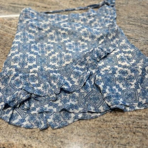 Blåvit omlottkjol från By Malina - Supersöt blåvit omlottkjol från By Malina med volangdetaljer och knytband i midjan. Kjolen har ett unikt mönster i blått på vit botten och är perfekt för varma dagar. Lätt och luftig känsla.